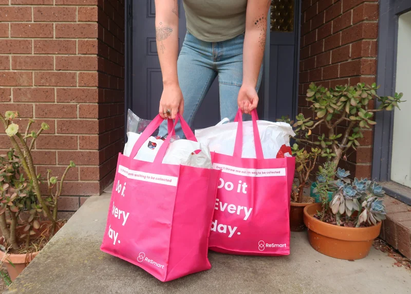 Person carrying two full pink ReSmart bags out of their front door